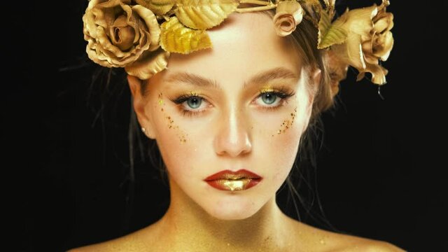 Fantasy portrait of woman, golden skin. Girl goddess in wreath, gold roses flowers. Beautiful face steel glitter art makeup eyes look at camera. black background. fashion model yellow shadows sparkles
