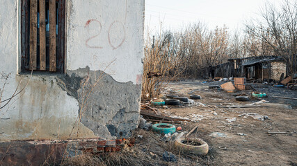 The wall of a dilapidated house with a boarded-up window, destruction and garbage in a poor...