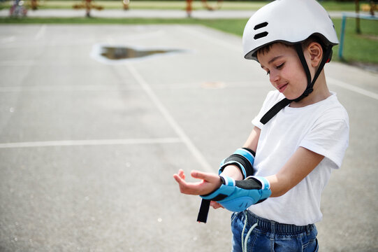 Boy skateboarder wearing safety helmet putting on protective armrests before skating