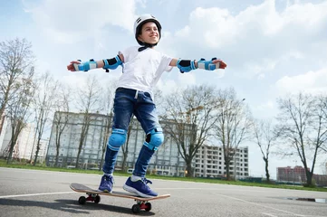 Poster Happy and smiling boy in protective gear and helmet keeps balance while riding a skateboard © Taras Grebinets