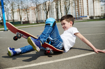 Little boy slipped and fell off the skateboard on the asphalt of the playground