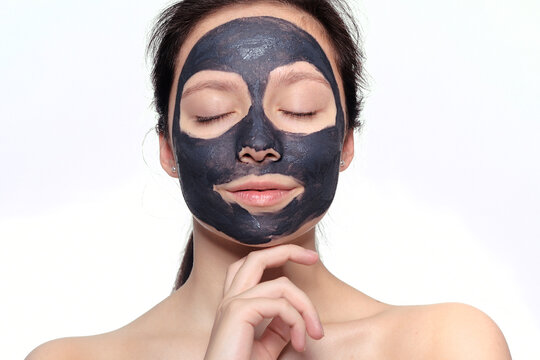 Teenager girl in a black mask, natural photo of a real mask on a young girl. Texture dark cream. Model on a white background smokes skin