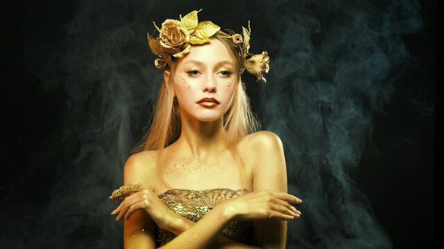 Fantasy portrait of woman glamour golden skin. Girl greek goddess in wreath, gold roses flowers. Beautiful face steel glitter sparklesart makeup. black background, white smoke. fashion model posing.