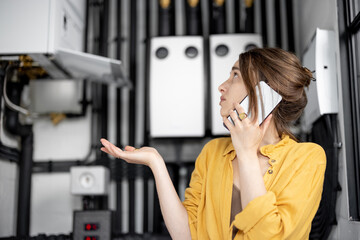 Fototapeta na wymiar Confused woman having problems with heating system at home, speaks on the phone trying to solve the problem. Concept of female incompetence in home appliances
