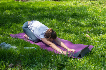 Woman doing yoga exercises in the park. Beautiful girl performs Child’s Pose. A girl on a purple...