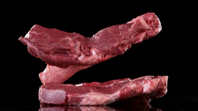 Flying pieces of raw beef steaks falling on table. Filmed on high speed cinema camera, 1000 fps.