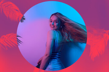A model in neon poses. Fashion photo of a girl in a swimsuit and shorts in pink-blue light. Girl on a background of tropical leaves summer photo. Beautiful blonde