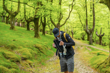 A young father with a yellow backpack walking with the newborn child in the backpack on a path in the forest heading to the picnic with the family