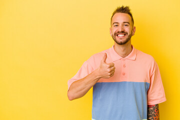 Young tattooed caucasian man isolated on yellow background smiling and raising thumb up