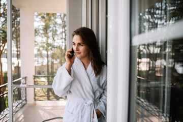 Obraz premium Brunette girl talking on phone standing on balcony in robe