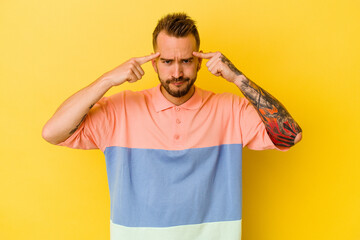 Young tattooed caucasian man isolated on yellow background focused on a task, keeping forefingers pointing head.