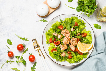 Green salad with baked fish at white table.