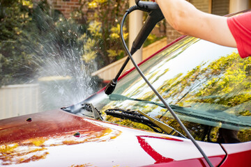 Washing a red car with high pressure washer cleaner.