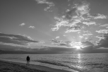 Hombre caminando por la orilla de la playa al amanecer mientras el sol aparece por entre las nubes