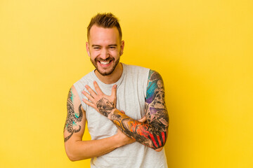 Young tattooed caucasian man isolated on yellow background laughs happily and has fun keeping hands...