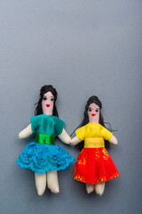Two handmade Brazilian cloth dolls holding hands on neutral gray background - obrazy, fototapety, plakaty