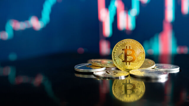 Bitcoin and other crypto coins on reflecting table. Blurred candlestick chart in the background. BTC known as digital gold asset in cryptocurrency world.