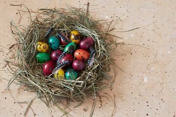 Fototapeta na wymiar Top view of wicker nest made with dry grass with colored Easter quail eggs on natural beige background with copy space. Happy Easter holiday. Flat lay