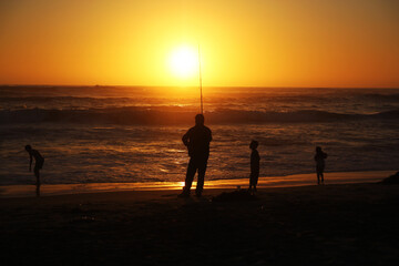 Fototapeta premium Silhouette of a fisherman with children on a beach during a sunset