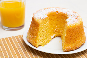 Orange cake with a little icing sugar and a glass of orange juice.
