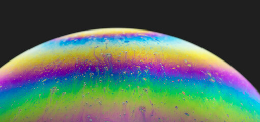 Blurred colourful soap bubble close up on black background. Creative background. Concept of space and creativity. Imitation of an unknown planet.