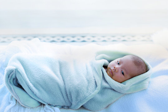 Asian Newborn Baby Wrapping With Blue Fabric On The Bed, Looking Someone