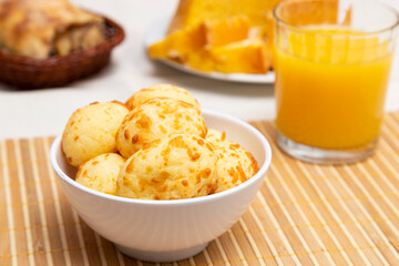 Pot with cheese bread and orange juice, on a table with orange cake.