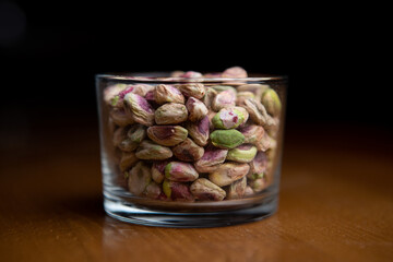 Peeled pistachios in clear glass on wooden table