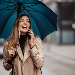 A beautiful young woman standing under an umbrella and talking on the phone.