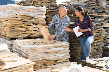 Confident woman shopper discussing with man quality of natural stone tiles at hardware store warehouse
