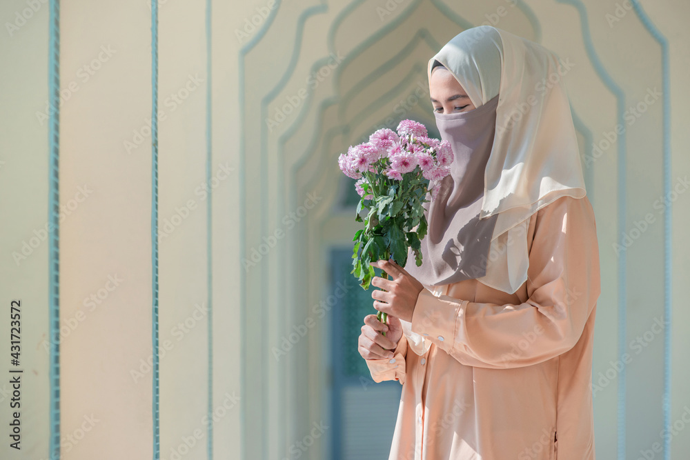 Wall mural Muslim woman in traditional clothes with Nigab holding bouquet of flower, looking at camera, copy space