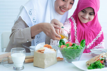 Asian Muslim mother or sister and her child preparing and tasting healthy food, women wearing hijab