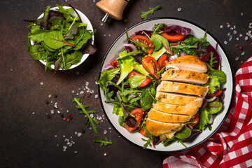 Green salad with baked chicken breast at kitchen table.