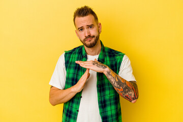 Young tattooed caucasian man isolated on yellow background showing a timeout gesture.