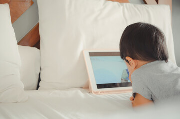 Little asian boy lying in bed and watch a story on touchscreen tablet,Early age education development. Video chat, video call.