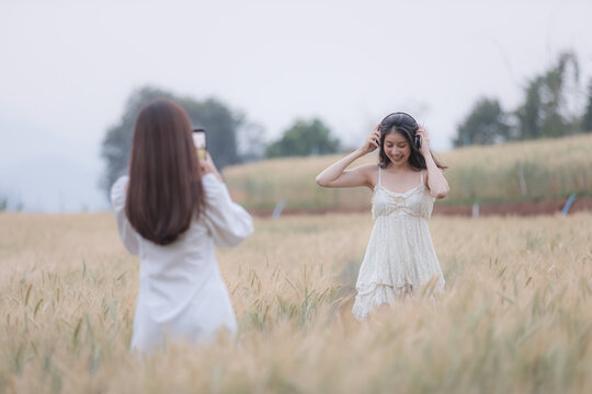 two young asian tourists girls strolling and taking pictures with smartphone in a barley demonstration plot