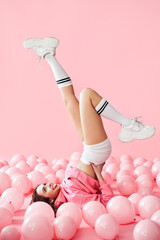 Young pretty woman have fun with legs up lying in pink balloons over pink pastel background