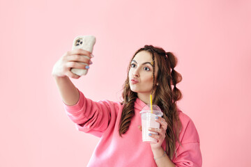 Young trendy woman making selfie portrait holding milkshake on pink background