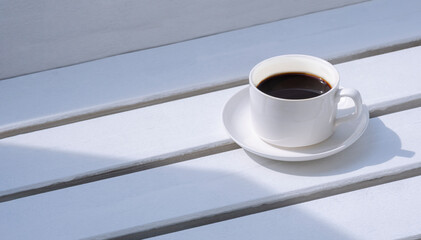 Morning sunlight on surface of black coffee in white ceramic cup on white wooden garden bench in vintage tone style