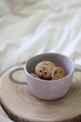 Bowl of chocolate chip cookies and wooden tray on a bed. Selective focus.