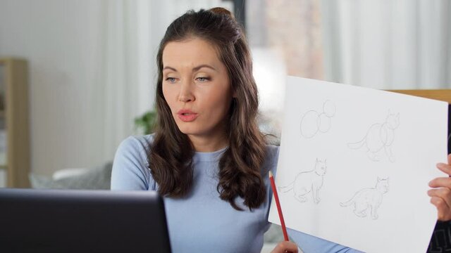 distant education, primary school and teaching concept - female teacher with laptop computer and tutorial picture of cat drawing having online class of arts at home