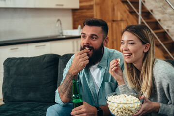 Couple in love drinking beer and eating popcorn at home