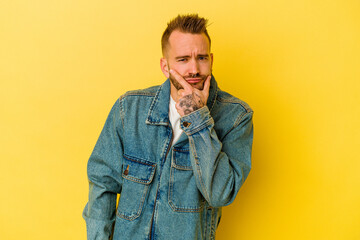 Young tattooed caucasian man isolated on yellow background contemplating, planning a strategy, thinking about the way of a business.