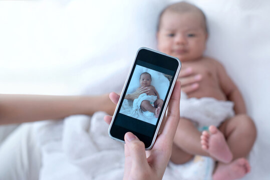 Mother taking a photo of her newborn baby by smartphone, selective focus