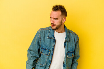 Young tattooed caucasian man isolated on yellow background looks aside smiling, cheerful and pleasant.