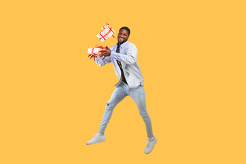 Fototapeta na wymiar Holidays and celebration time. Overjoyed african american guy holding gift boxes and jumping on yellow background