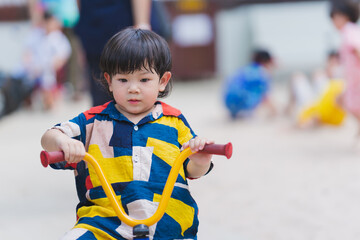 Adorable 2-3 year old Asian boy riding tricycle at playground. Baby was sweating on his face due to...
