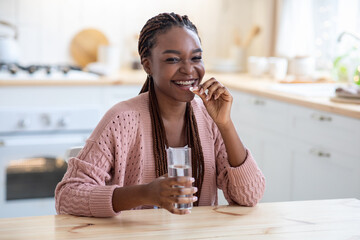 Cheerful Young African American Lady Taking Beauty Supplement Pill In Kitchen - obrazy, fototapety, plakaty