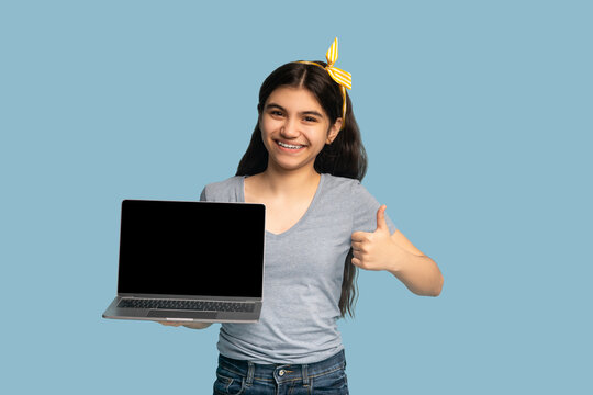 Positive Indian Teenager Holding Laptop Computer With Blank Screen And Showing Thumb Up Gesture On Blue Background