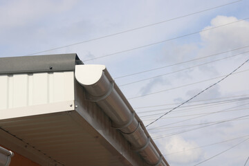 Part of roof with plastic gutter against blue cloudy sky